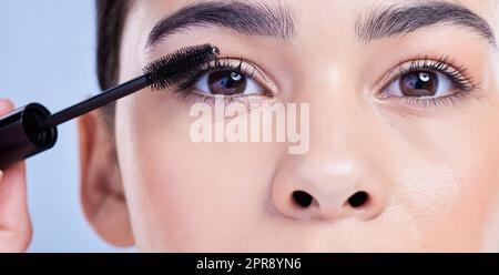 Closeup portrait of a beautiful young mixed race woman with glowing skin posing against blue copyspace background. Hispanic woman with natural looking eyelash extensions applying mascara Stock Photo