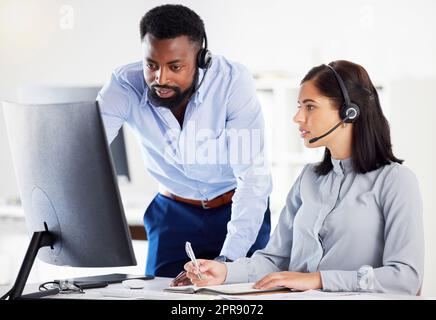 Young african american call centre telemarketing agent training new caucasian assistant on a computer in an office. Team leader troubleshooting solution with intern for customer service and sales support. Colleagues operating helpdesk together Stock Photo