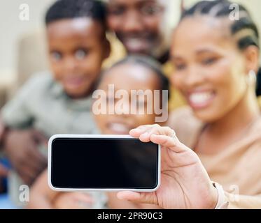 Say cheese. an unrecognisable family sitting on the sofa together at home and taking selfies on a cellphone. Stock Photo