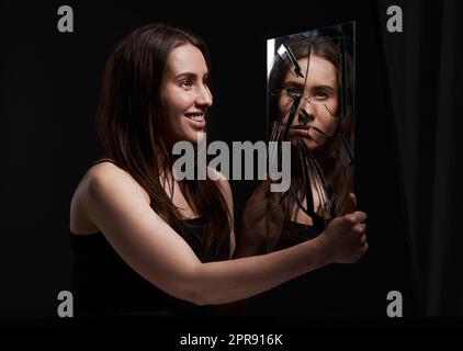 You dont know me. a creepy woman grinning at her reflection in a broken mirror. Stock Photo
