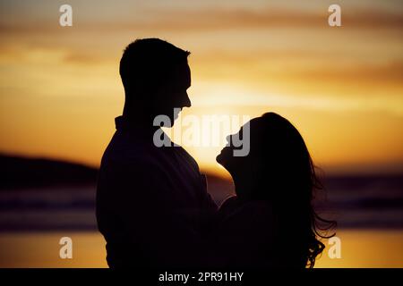 Silhouette couple enjoying romantic moment standing face to face looking into eyes at sunset. Unknown boyfriend and girlfriend feeling in love while bonding at the beach Stock Photo