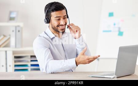 Businessman working in a call center. Customer service agent talking to a customer. Sales rep wearing a headset using a laptop. IT assistant giving advice. Call center worker using his computer Stock Photo