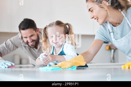Little girl helping her parents clean. Caucasian family cleaning their kitchen together. Happy family doing housework together. Family keeping their kitchen counter clean and hygienic. Stock Photo