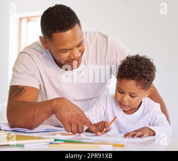 Mixed race boy learning and studying in homeschool with dad. Man helping his son with homework and assignments at home. Parent teaching child to colour and write at home during lockdown Stock Photo