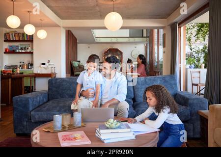 Father using a laptop at home with children. A happy dad online with his a and daughter. Young mixed race man with a little boy and girl using a computer, doing homework, learning and working remote Stock Photo