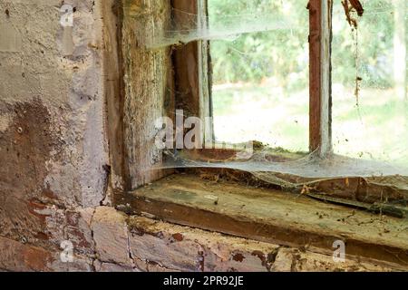 Interior view of an ancient house in need of TLC. An old window with dust and spiderwebs in an abandoned home inside. Architecture details of a windowsill frame with damaged rustic textures. Stock Photo