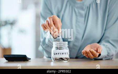 Savings, budget and economical woman putting coins in a jar at home. Closeup of woman calculating her expenses and saving money for future investment managing her house finances Stock Photo