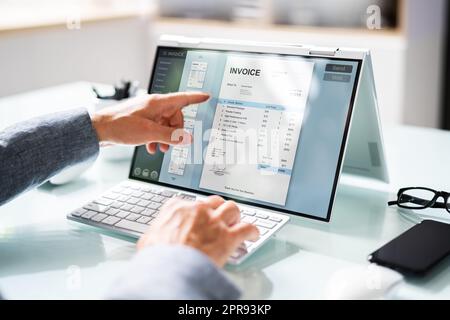 Businessperson Analyzing Invoice On Laptop Stock Photo