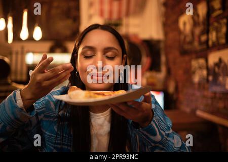 Hungry woman with delicious pizza, food or consumables at a bar, restaurant or diner at night. One happy and casual girl, foodie or tourist enjoying a dinner meal at a local trendy location Stock Photo