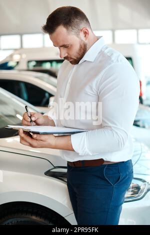 Sign on the dotted line. a car salesman writing on a clipboard. Stock Photo