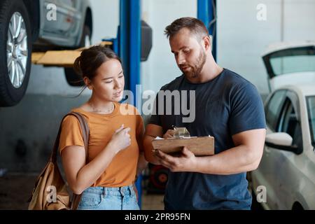 An informed auto-repair customer is a happy customer. a woman talking to a mechanic in an auto repair shop. Stock Photo