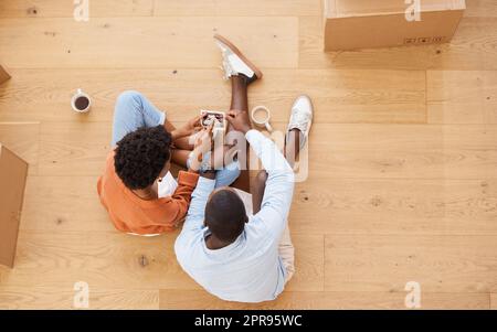 Opening up a new chapter of our lives. a young couple sitting on the floor while looking at an ultrasound picture at home. Stock Photo