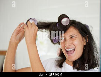 I didnt expect it to be so complicated. a young woman taking rollers out of her hair. Stock Photo