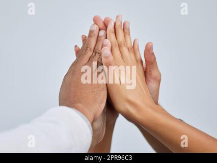We are stronger when we stand together. Closeup shot of a group of people giving each other a high five against a white background. Stock Photo