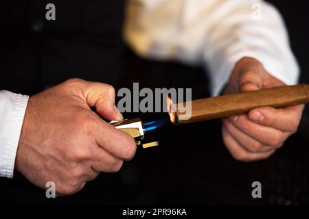 Treat yourself to the finer things in life. an unrecognizable man lighting a cigar with a lighter. Stock Photo