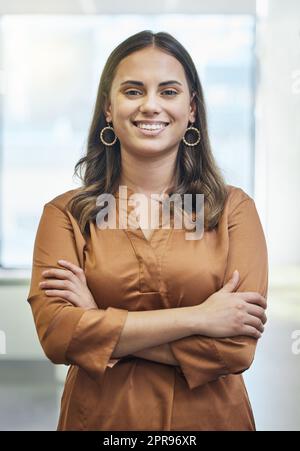 Proud of how far Ive come. Cropped portrait of an attractive young businesswoman standing with her arms folded in the office. Stock Photo