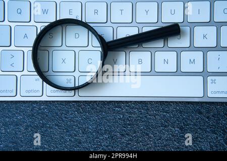 Magnifying glass and keyboard. Discover how to use SEO to improve your search engine ranking. Stock Photo