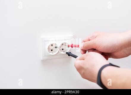 Measuring the voltage in the socket with a professional digital multimeter. Profession electrician, the process of installing sockets. Close-up, selective focus, noise. Stock Photo