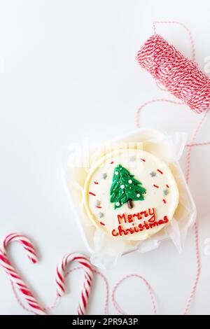 Christmas cake with the inscription merry christmas, decorated with icing, on a white background with candy canes and a red thread for gifts, preparation for the holiday. Stock Photo