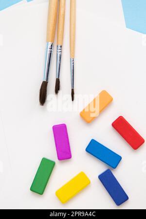 Multi-colored bright paints, watercolor brushes of different sizes lie together on watercolor paper on a blue background. Drawing lessons. Stock Photo