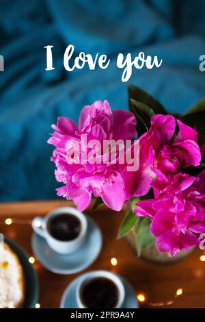 Beautiful morning Vanilla cheesecake, coffee, blue cups, pink peonies in a glass vase. Inscription I love you. Stock Photo
