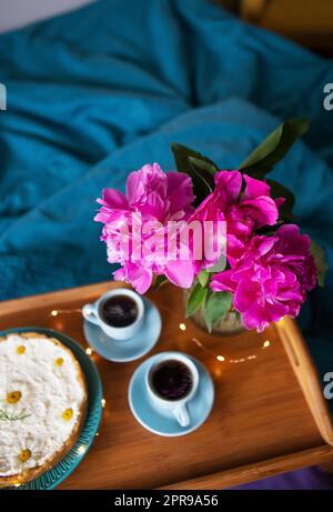 Beautiful morning Vanilla cheesecake, coffee, blue cups, pink peonies in a glass vase. Stock Photo