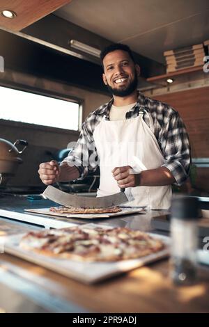 Your pizza is almost ready. a handsome young man standing and preparing a freshly made pizza for takeaway in his restaurant. Stock Photo