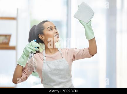 Getting my shiny windows back. a young woman cleaning a glass window at home. Stock Photo