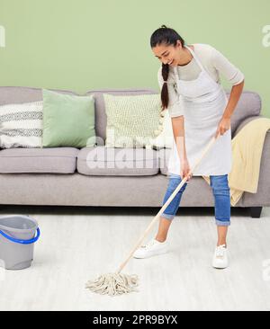I want to see my reflection on the floor. Full length shot of an attractive young woman standing and mopping her living room. Stock Photo