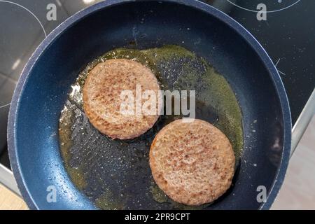 Two burger patties burger meat sizzling in hot pan with fat and oil as delicious selfmade hamburger bbq meatballs as unhealthy fast food lunch with lots of calories and cholesterol in frying pan Stock Photo
