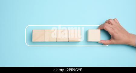 A woman's hand holds wooden cubes on a blue background. Stock Photo