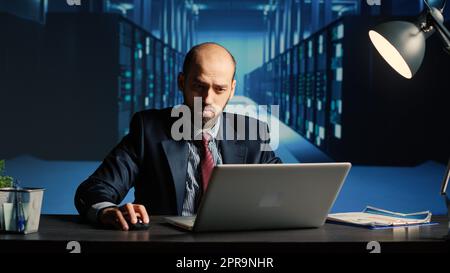 Data center technician feeling tired working in server room, doing cloud computing digitalization for database storage. Man engineer inspecting computer system and hardware, IT industry. Stock Photo