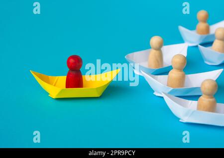 Red wooden figure on yellow paper ship origami leading the rest. Stock Photo