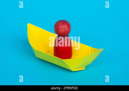 Red wooden figure on yellow paper ship with blue background. Stock Photo
