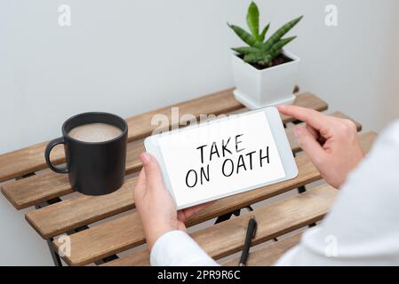 Hand writing sign Take On Oath. Word Written on A solemn appeal to a deity Speak the truth Make a Promise Woman Holding Tablet With Recent Data On Table With Coffee, Pen And Plant Stock Photo