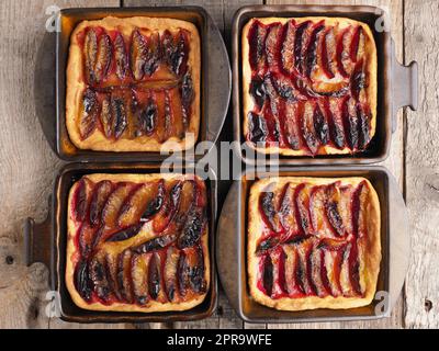 Freshly baked plum cake in ceramic bowls on a rustic kitchen table, top view Stock Photo