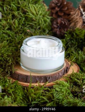 Opened glass jar full of cream on wooden piece between green moss, closeup, mockup Stock Photo