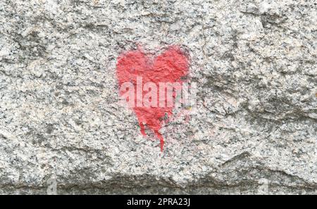 A small generic red heart symbol painted on a wall, heart icon front view, closeup, urban area, architecture, building side spray painted heart. Love, Stock Photo