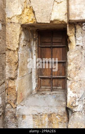 Wooden grunge closed window with wrought iron grid in stone bricks wall Stock Photo