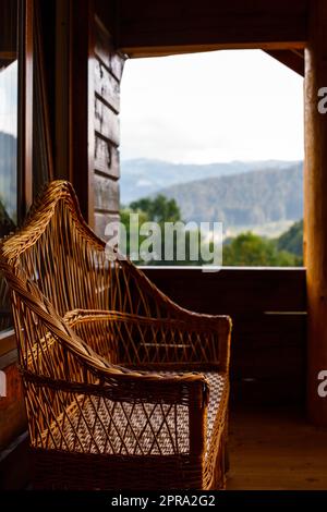 Wicker chair on the terrace of a wooden cottage overlooking the mountain forest. Stock Photo