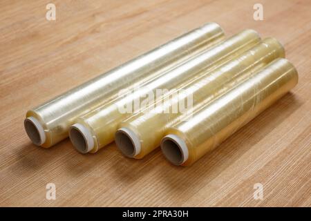 Close up on wooden table lies four rolls of transparent food film on cardboard spool. Stock Photo