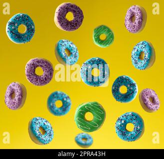 Multi-colored donuts sprinkled with sugar sprinkles fly on a yellow background Stock Photo