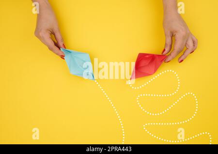A woman's hand holds paper boats with different trajectories. Stock Photo