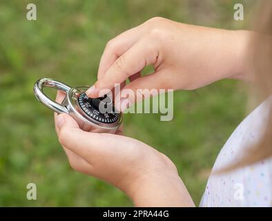 Child unlocking a simple closed coded lock, holding a code padlock in hands. Password cracking, encryption and decryption, hacking, cracking abstract Stock Photo