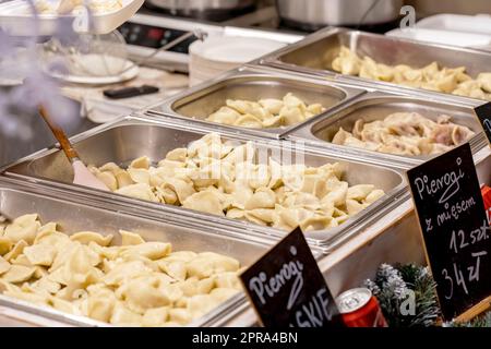 Metal containers full of freshly cooked delicious hot steaming Polish pierogi, restaurant, traditional festive market food catering service simple con Stock Photo