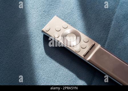 One single simple silver premium smart TV remote control laying on a sofa, couch, object in the sun, detail, closeup, nobody Watching TV symbol, digit Stock Photo