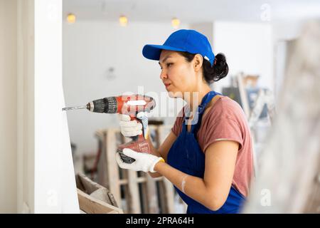 Woman builder using drill to bore hole in wall Stock Photo