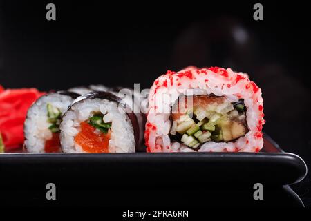 Rice Japanese rolls of Uramaki and Maki with salmon, cucumber, and red caviar on a black plate. Stock Photo