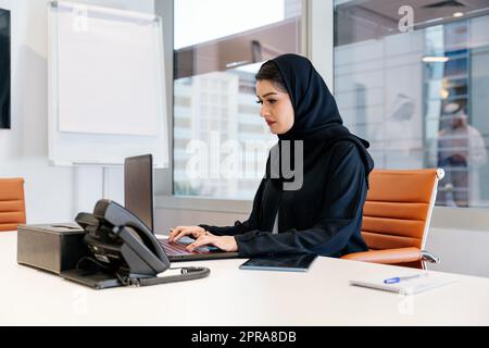 Portrait of beautiful middle-eastern corporate businesswoman wearing abaya and working in the office in Dubai Stock Photo