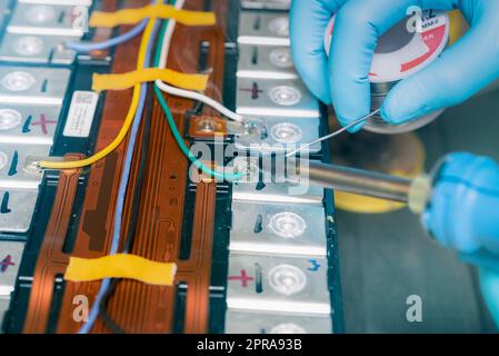 Technician use soldering iron to solder metal and wire of lithium-ion rechargeable battery. Repair module of Li-ion battery. Engineer hand holds soldering iron and tin-lead to solder electronic board. Stock Photo